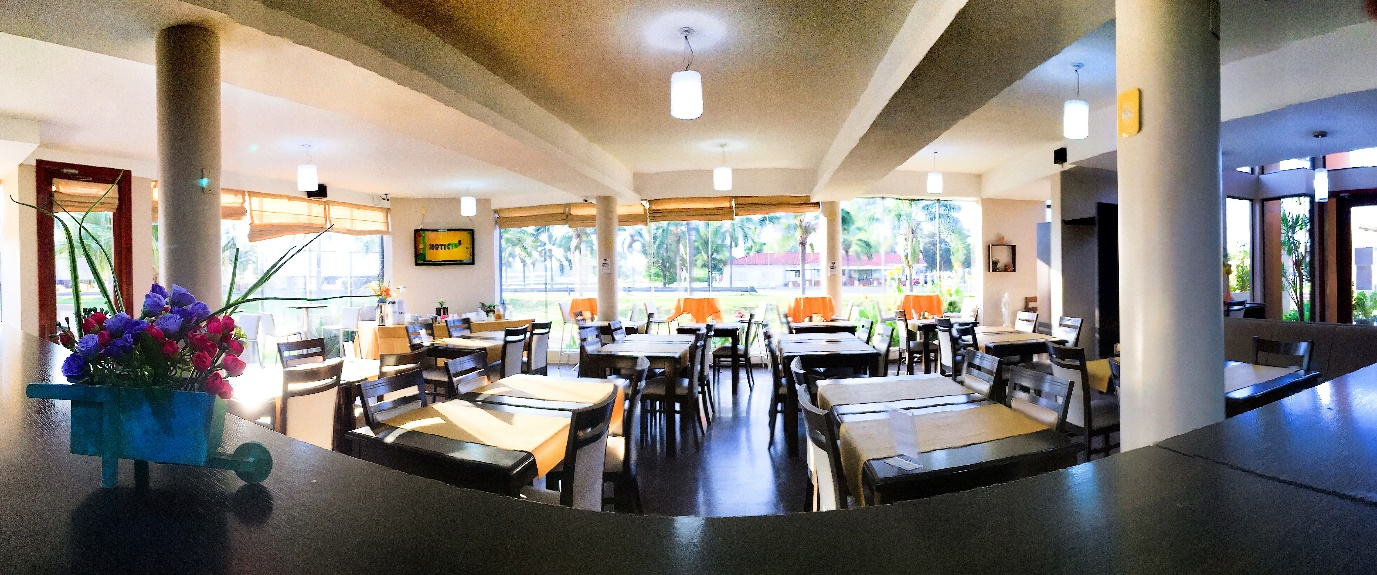Vista panorámica del interior de un restaurante con mesas, sillas y grandes ventanales que dan a un jardín.
