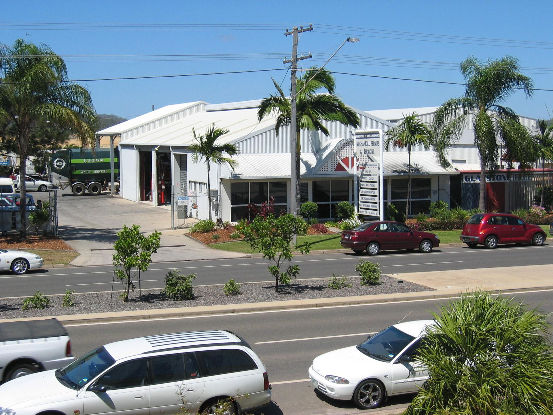 Cars parked near a building with palm trees and a sign, sunny day.— Gladstone Fleet Maintenance In Gladstone, QLD