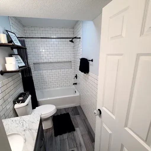Modern bathroom with subway tile, dark fixtures, and gray wood-look floors.
