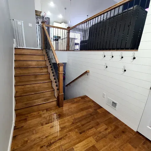 Wooden stairs leading up to a second-floor railing. White-paneled wall with coat hooks and door.