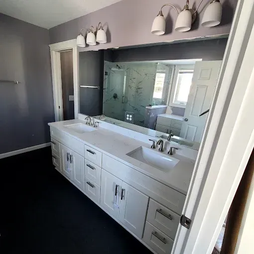 Bathroom with white vanity, dual sinks, large mirror, gray walls, and dark floor.