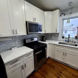 Bright kitchen with white cabinets, stainless steel appliances, and a window overlooking a snowy scene.