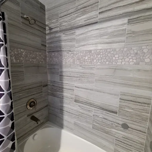 Bathroom with gray and white striped tile, a decorative pebble border, and chrome fixtures.