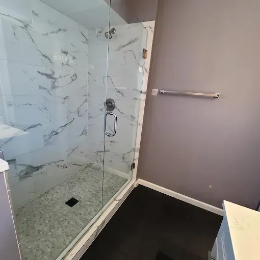 Shower with marble-look tiles, pebble floor, glass door, and purple walls.