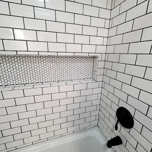 White subway tile bathroom with a recessed shelf of honeycomb tile and black fixtures.