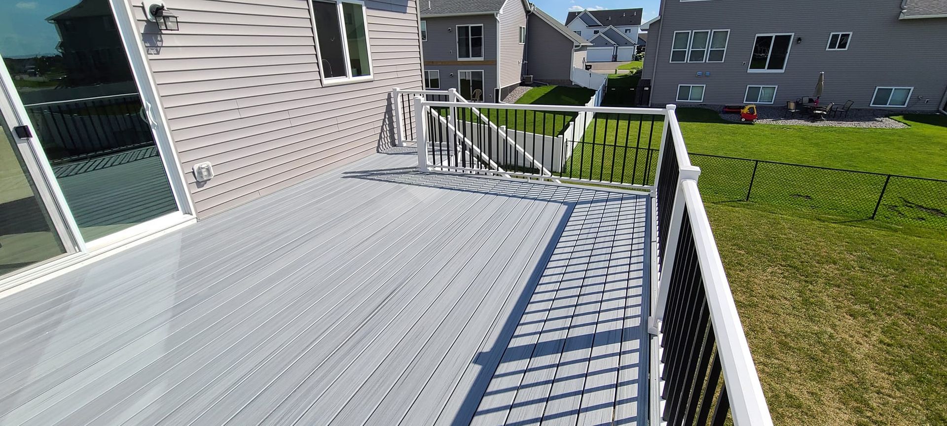 Gray composite deck with black railing, overlooking a grassy yard, and a house in the background.