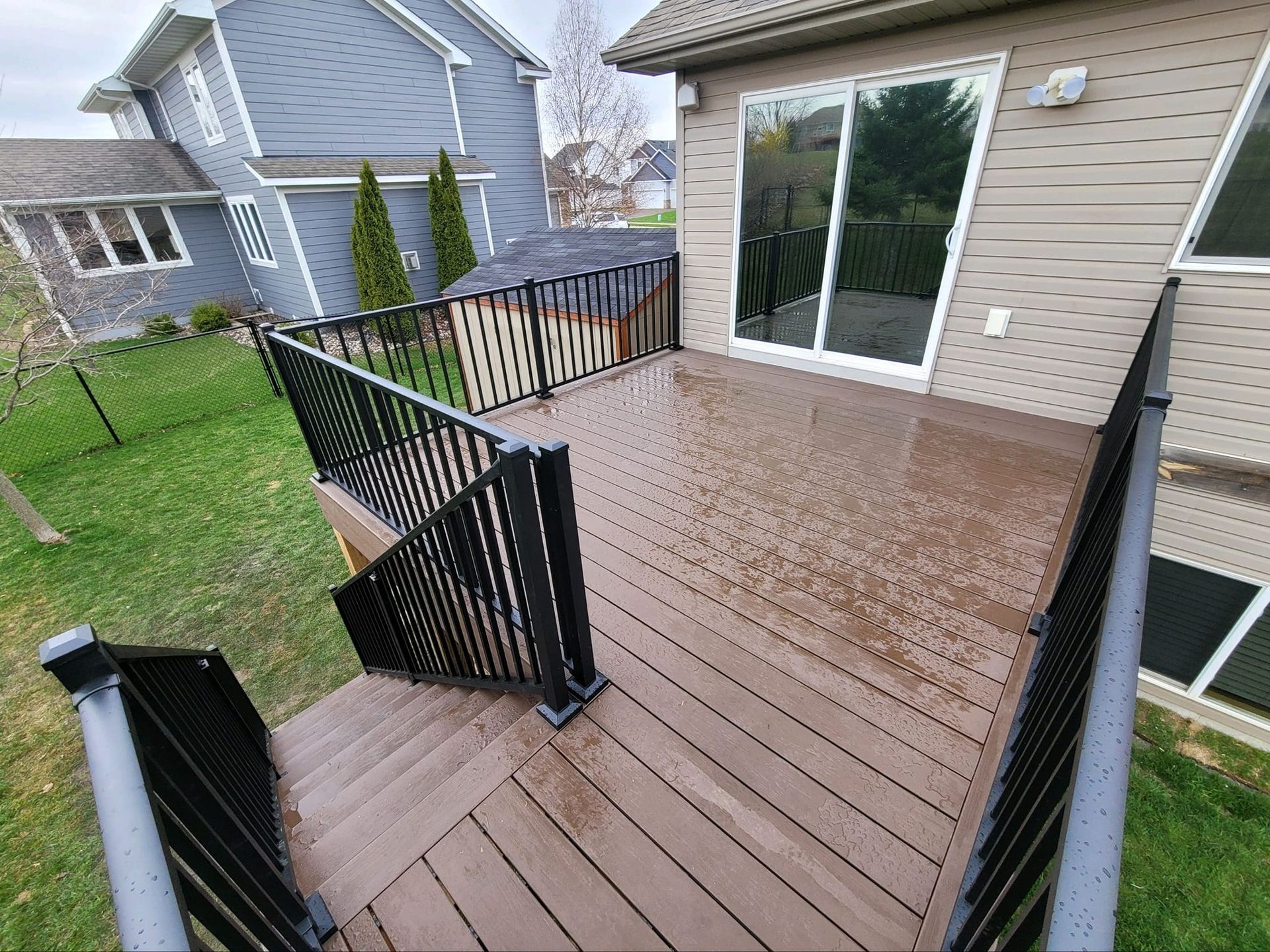 Brown deck with black railings next to a beige house with a sliding glass door.