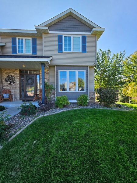 Two-story beige house with blue shutters and a lush green lawn on a sunny day.