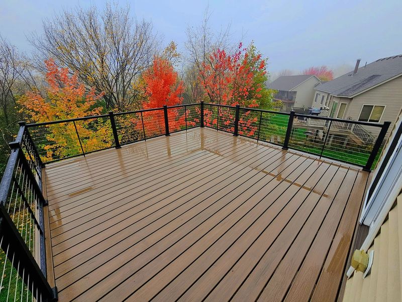 Wooden deck with black railing, overlooking fall foliage on a foggy day.