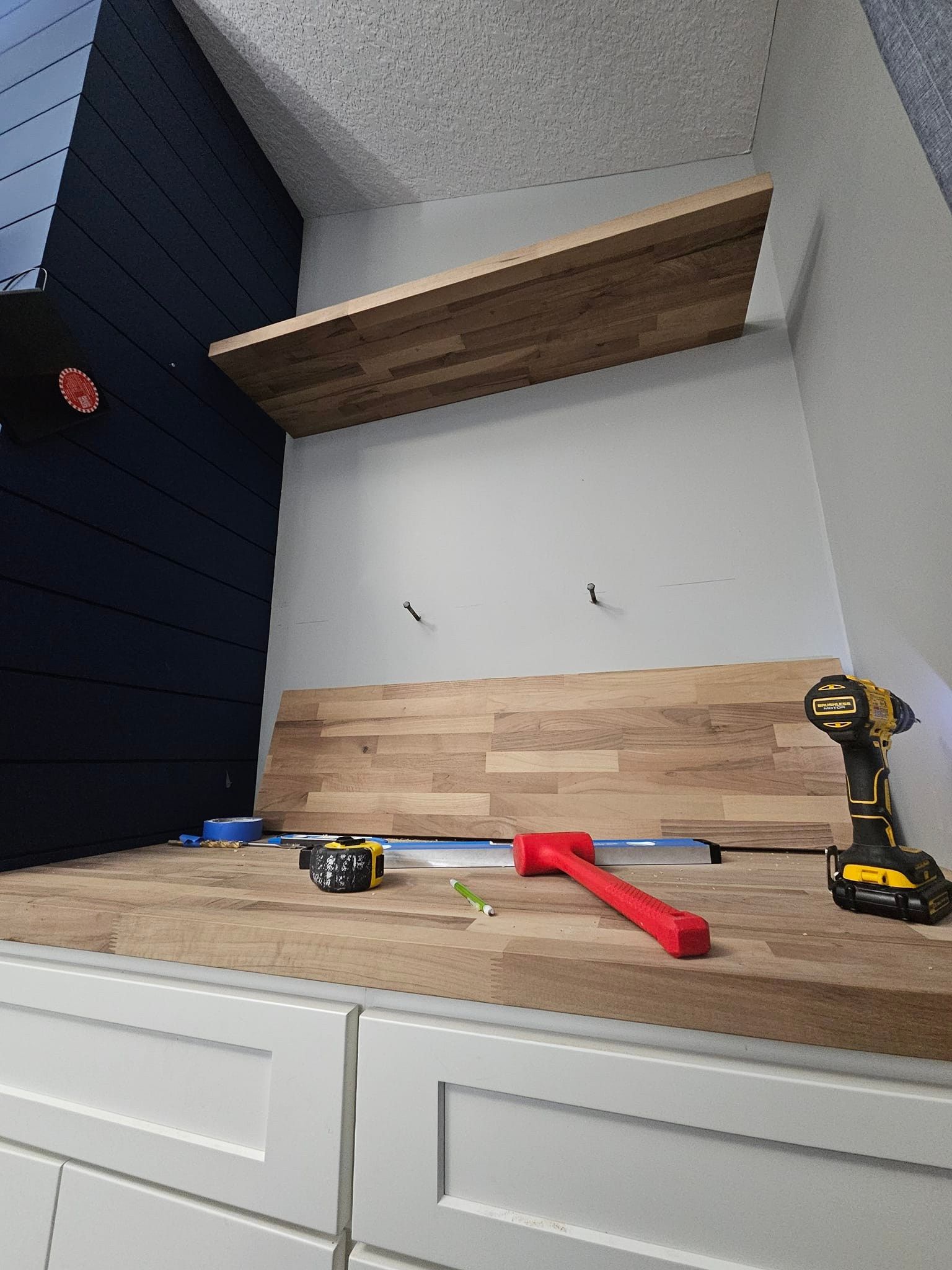 Wood planking installation on a white cabinet, tools visible. Dark blue wall on the left.