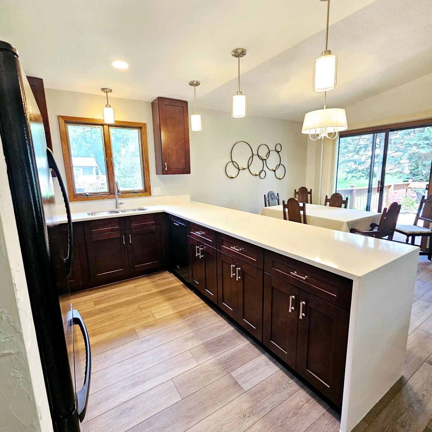 Kitchen with dark cabinets, white countertops, and wood floors; opens to a dining area with sliding glass doors.