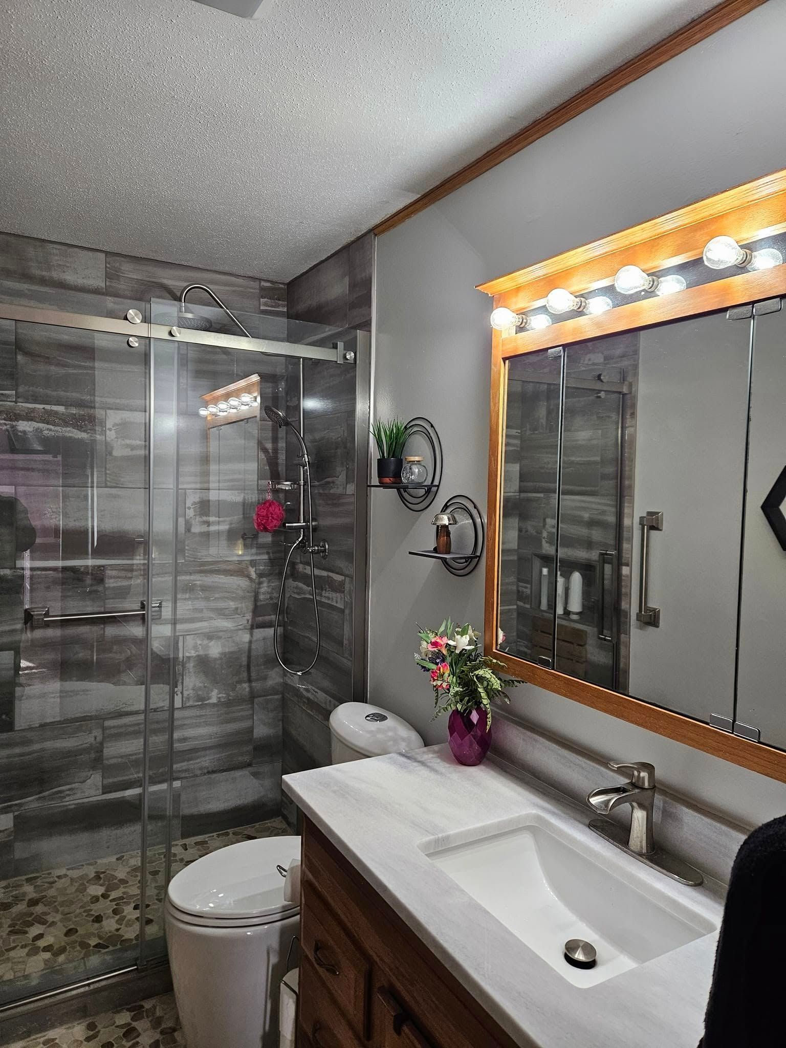 Modern bathroom with gray tile, glass shower, and wooden vanity.