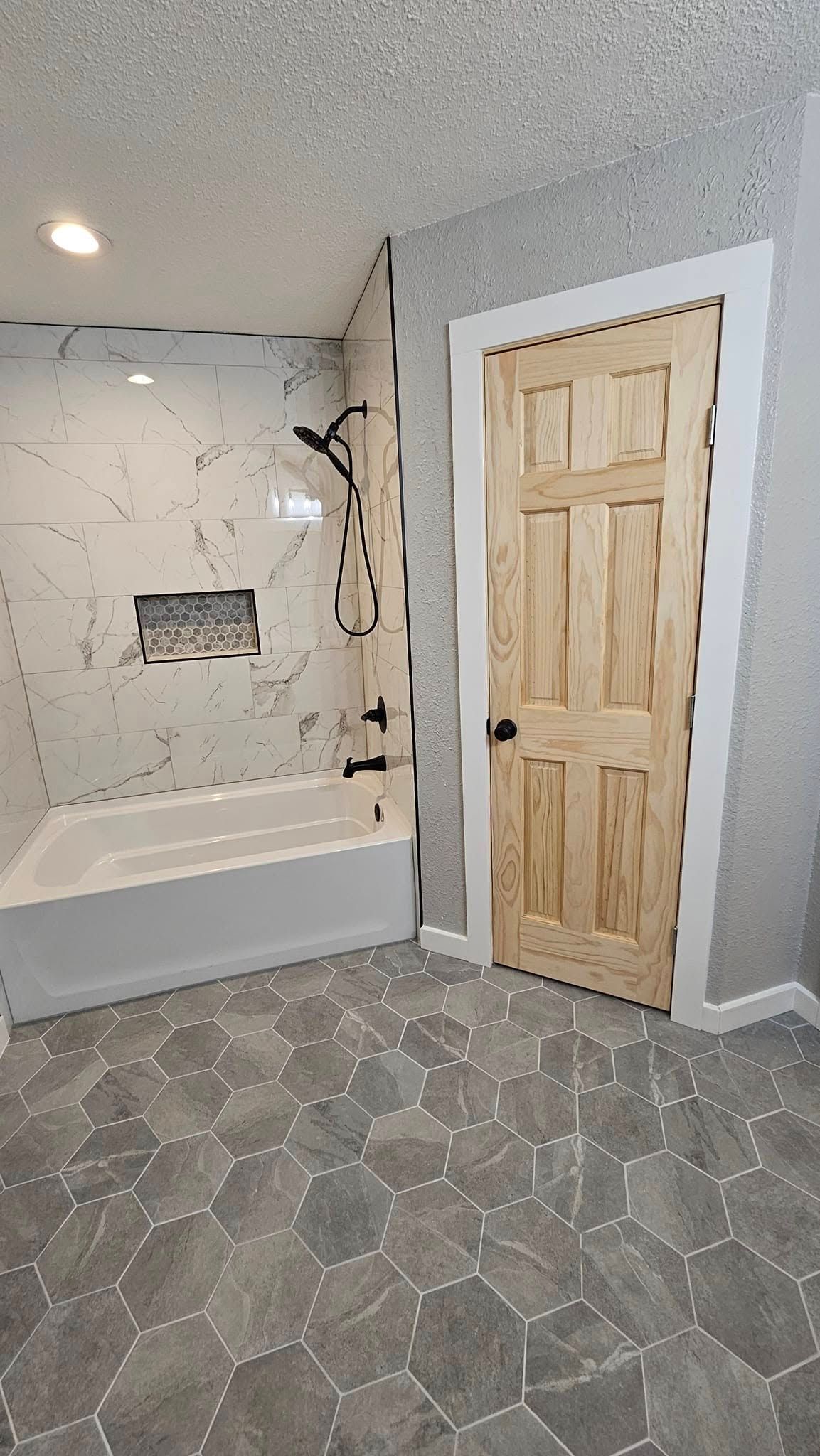Bathroom with marble tiled shower, hexagon floor tiles, and wooden door.