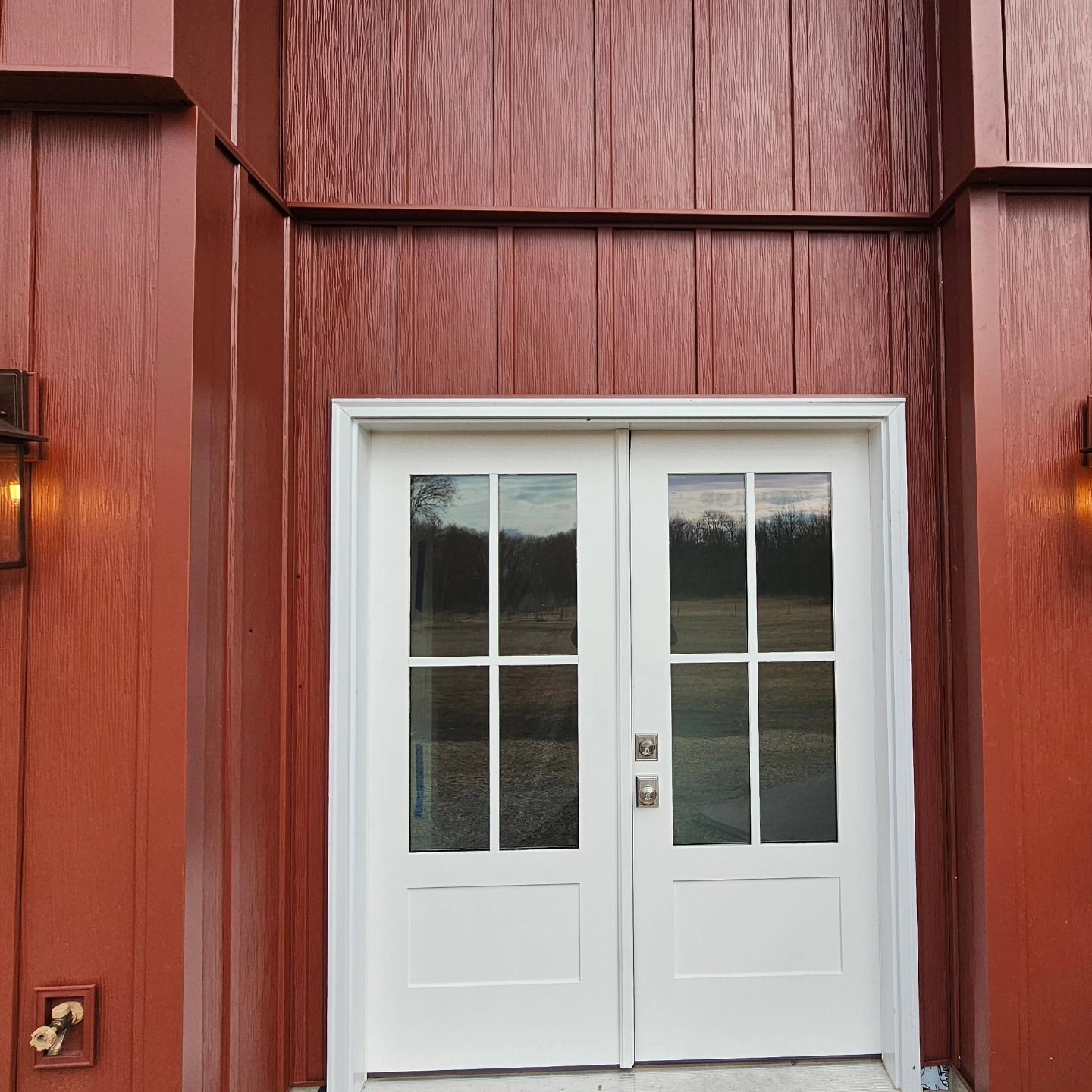 White double doors with glass panels, framed by reddish-brown vertical siding.