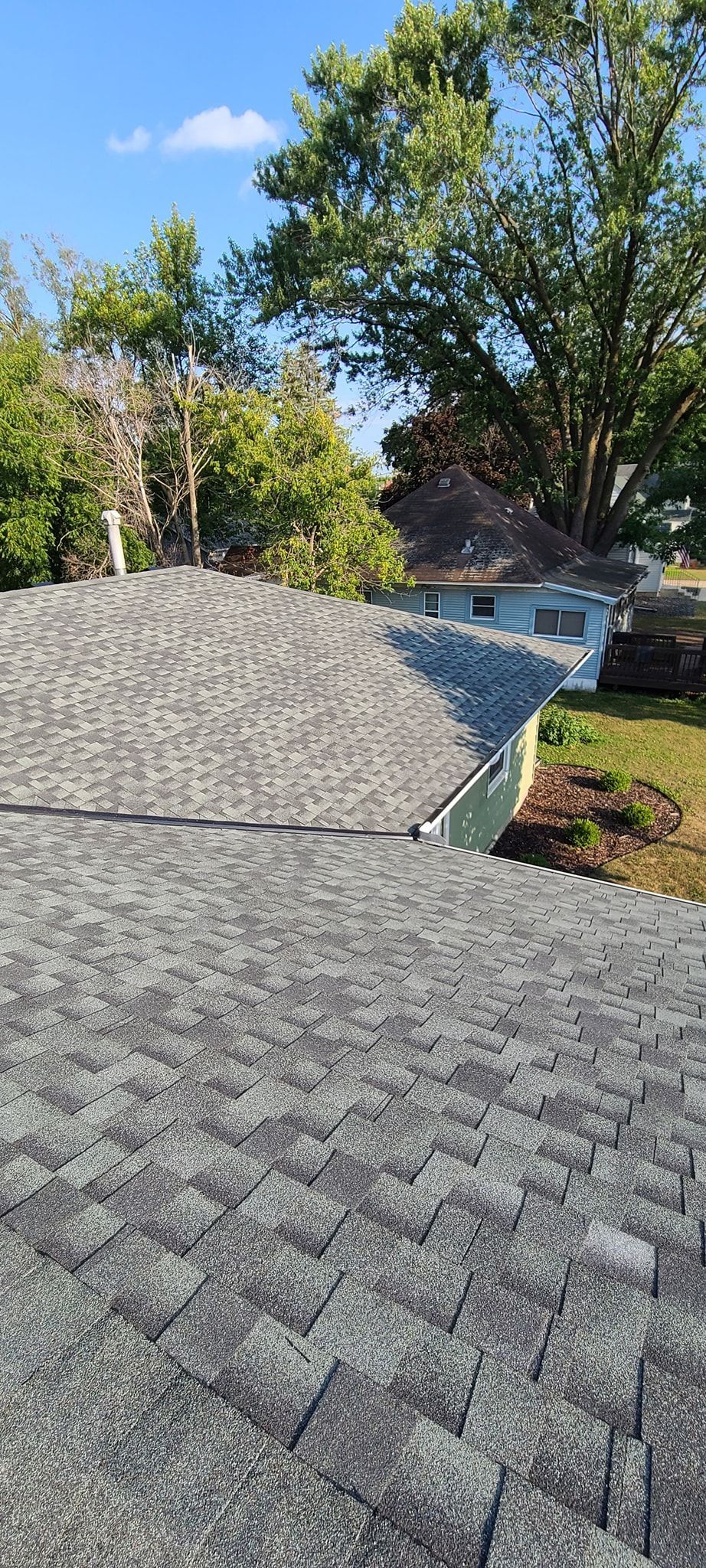 A rooftop covered in gray pavers with trees in the background under a blue sky.