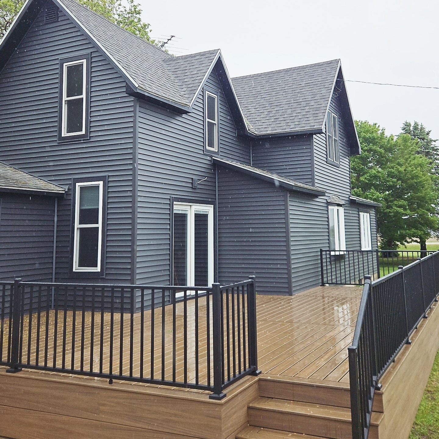 Dark gray house with wooden deck and black railing.