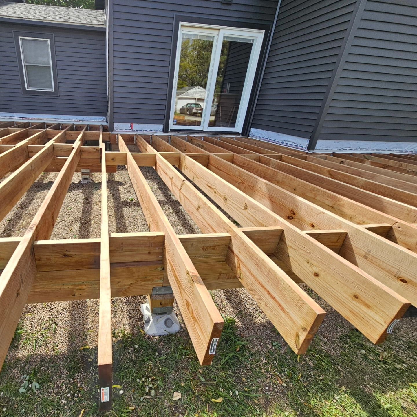 Wooden deck frame under construction near a dark gray house with a sliding glass door.