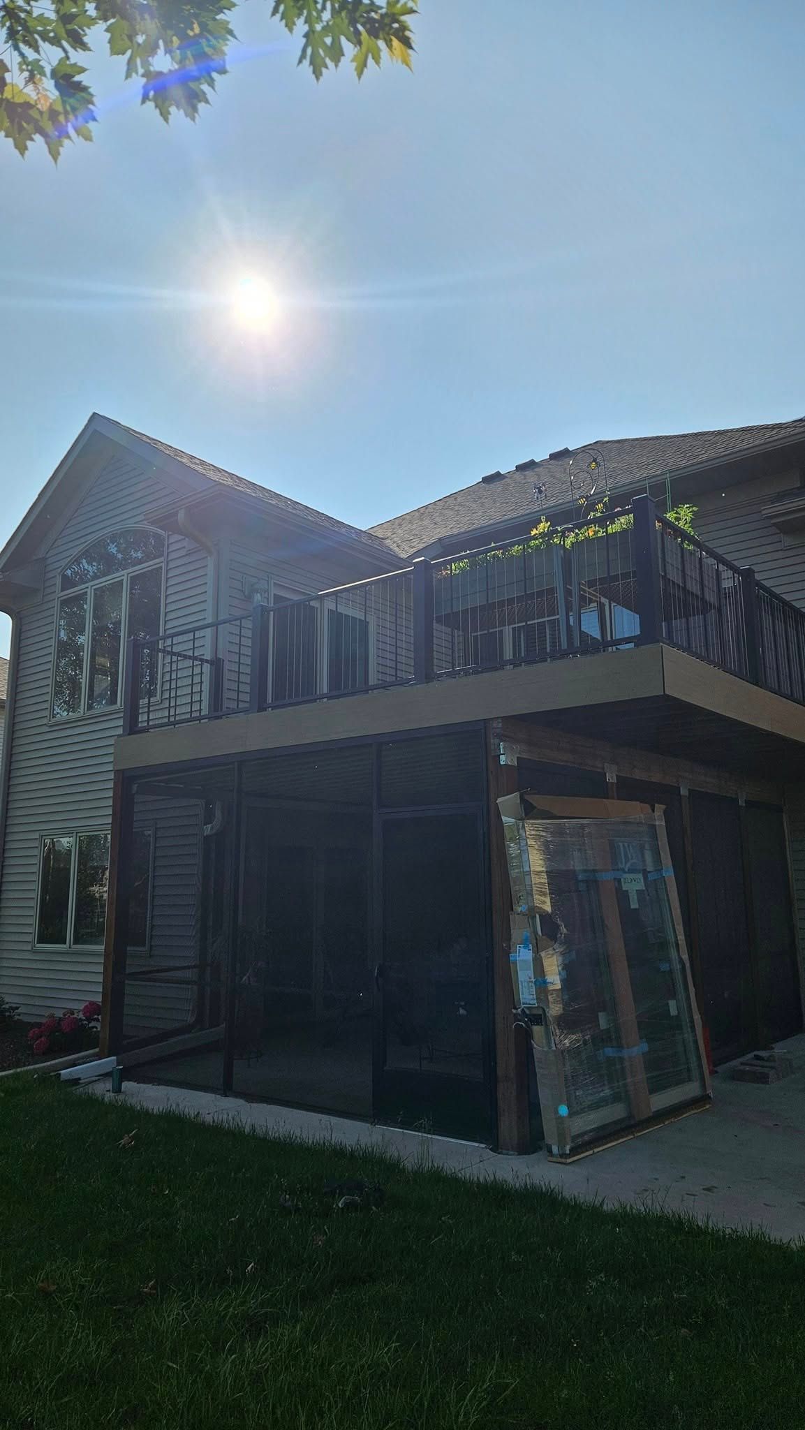Two-story house with a deck, sun shining. Dark siding, brown deck railings, and screened porch.