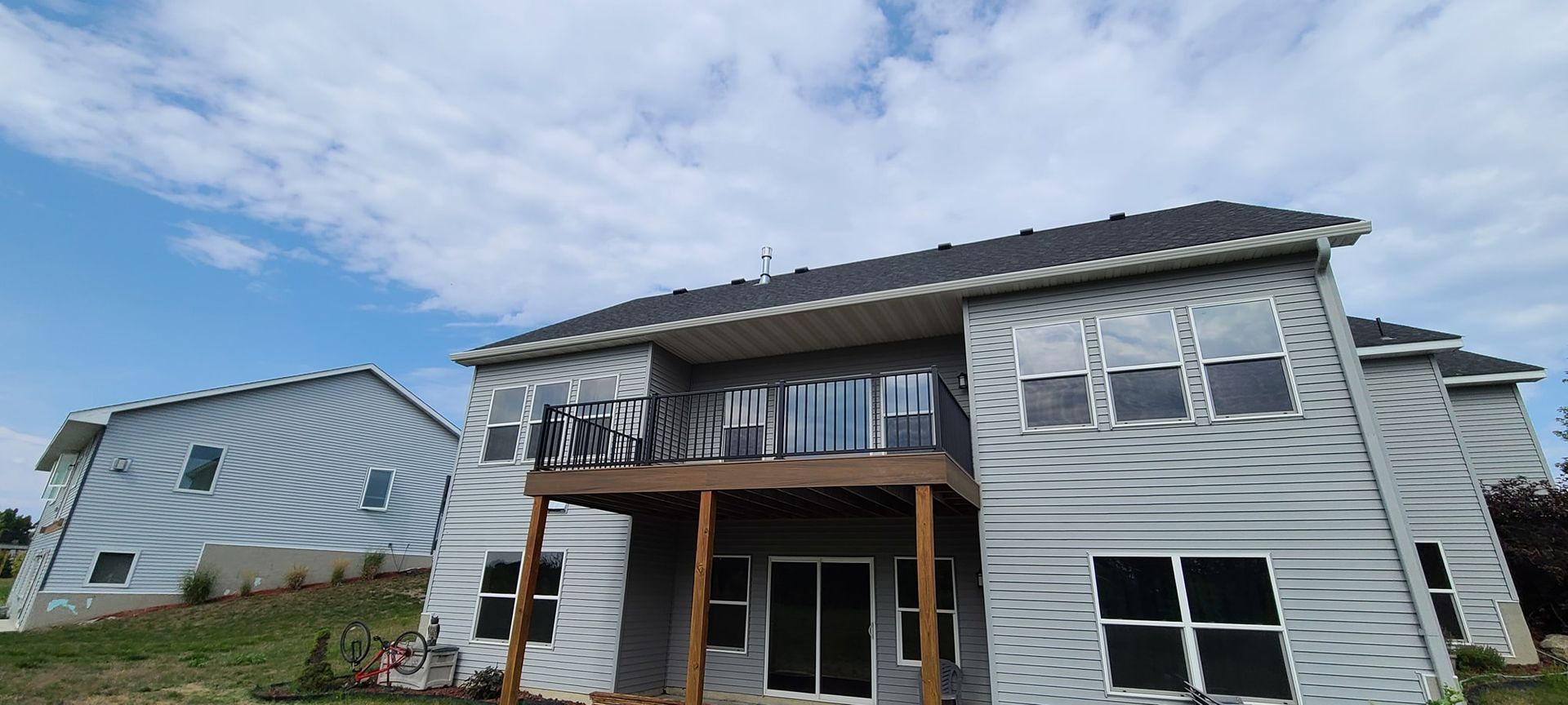Gray-sided house with deck, blue sky with clouds in the background.