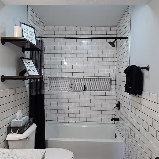 A modern bathroom with white subway tiles, black fixtures, and wooden shelves.