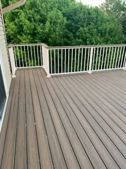 A brown composite deck with white railing, overlooking a lush green tree line.