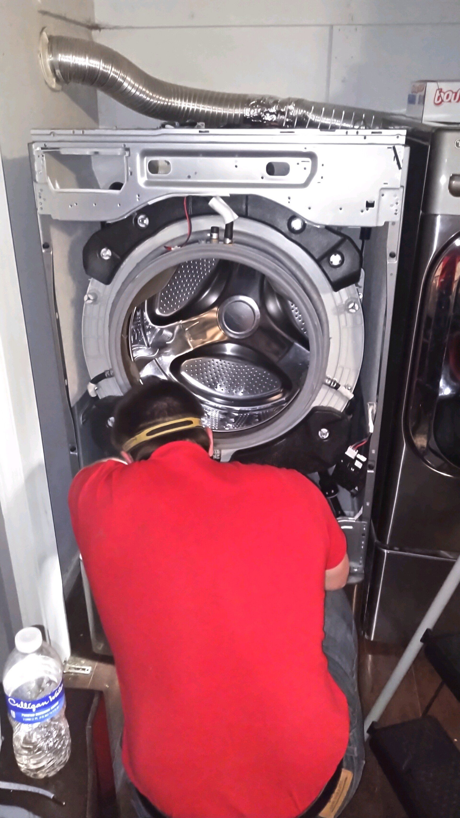 A man in a red shirt is repairing a washing machine.