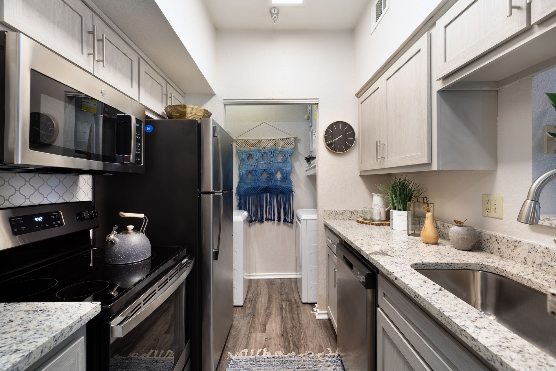 A modern kitchen with stainless steel appliances, light gray cabinets, and granite countertops.
