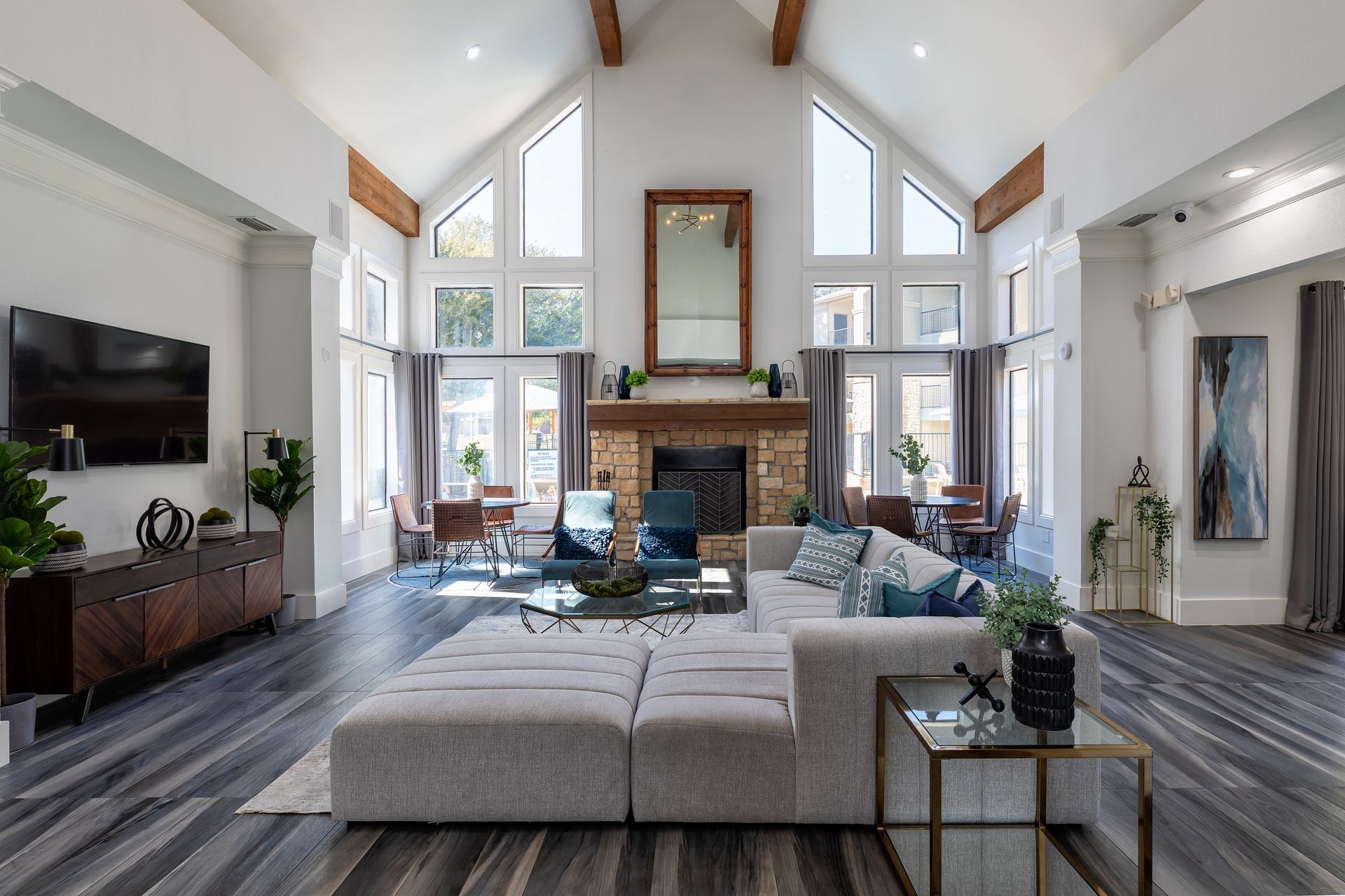 Modern clubhouse with a fireplace, large windows, sectional sofa, and wood beams.