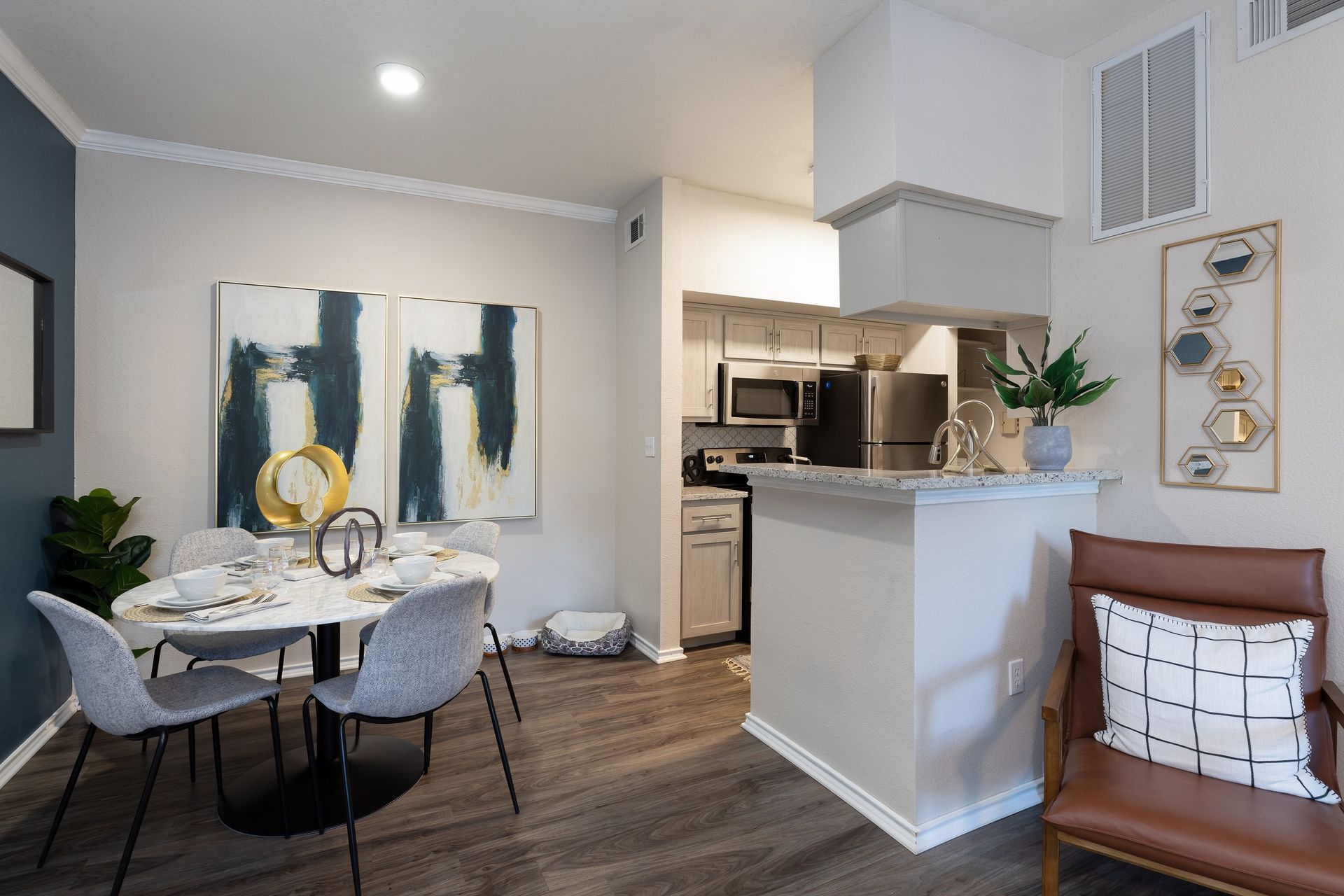 Dining area in apartment with table, chairs, artwork, and partial kitchen.