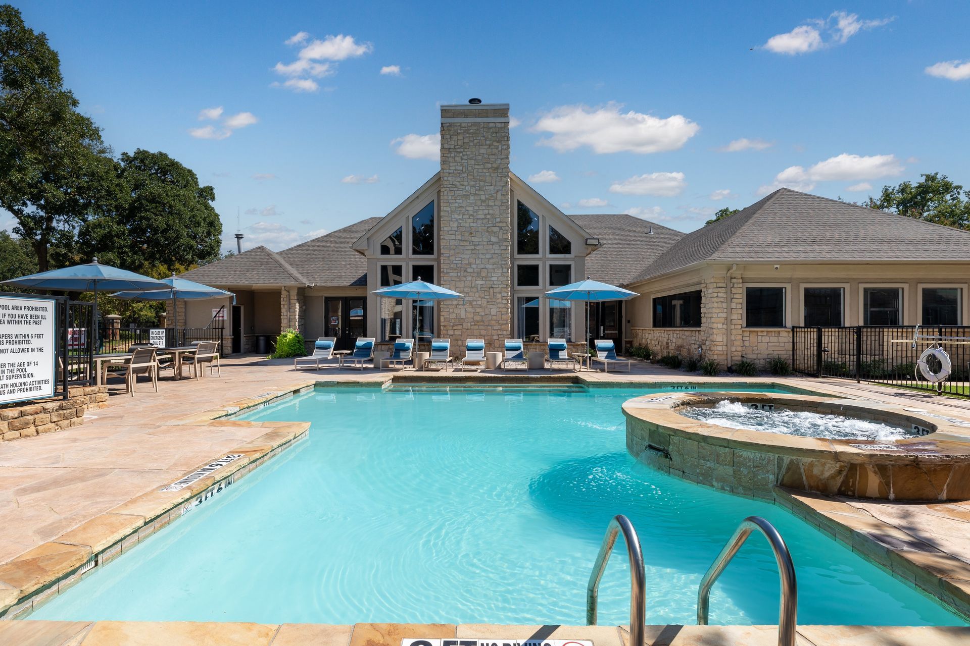 Swimming pool with lounge chairs, umbrellas, and a stone building in the background.