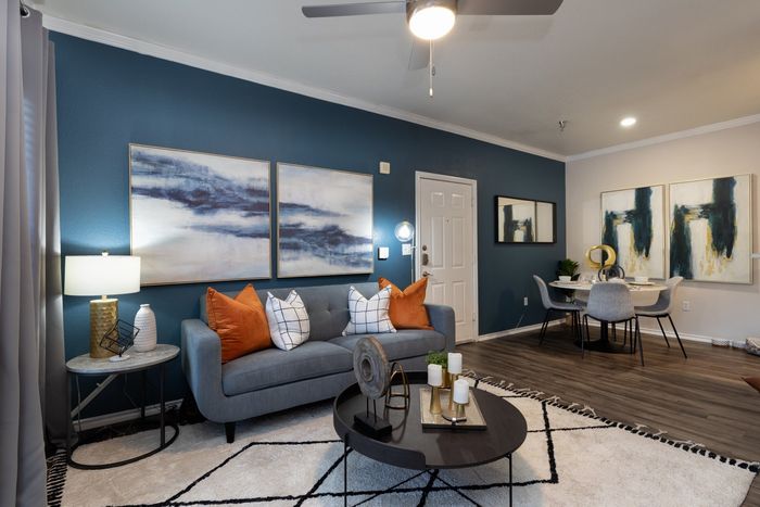 Living room with blue wall, gray sofa, art, and dining area.