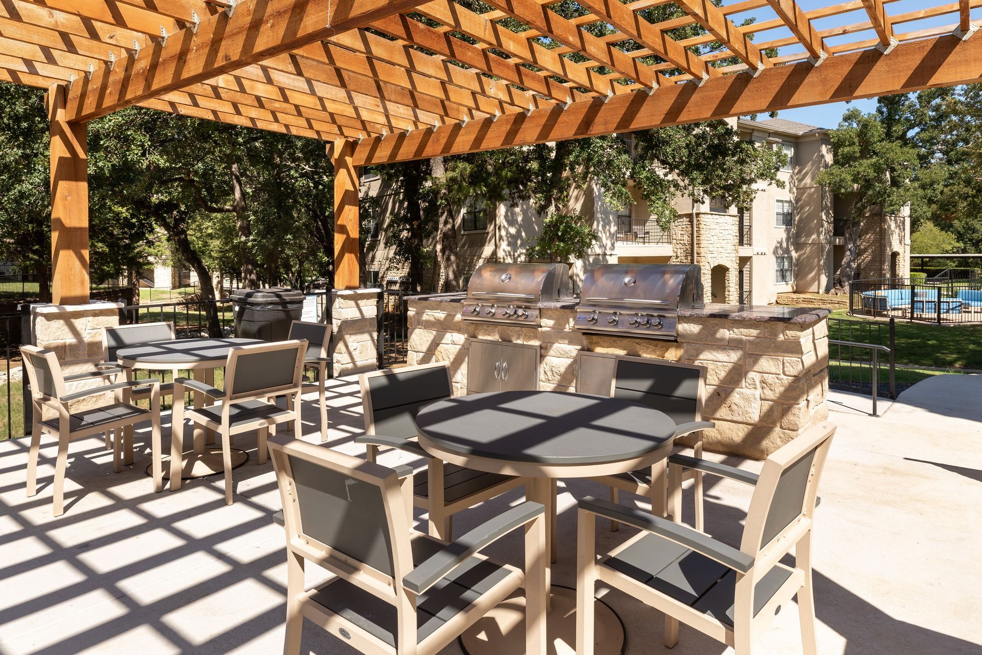 Outdoor grilling and dining area with a pergola, tables, chairs, and stainless steel grills.