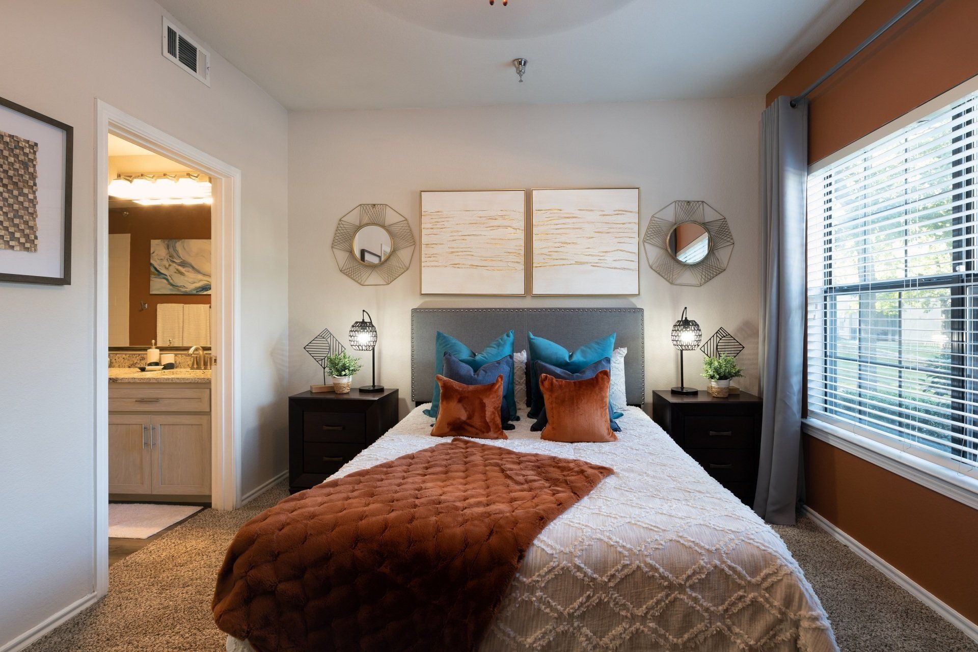 Bedroom with a bed, nightstands, and art. Warm colors, including orange and blue, are featured.