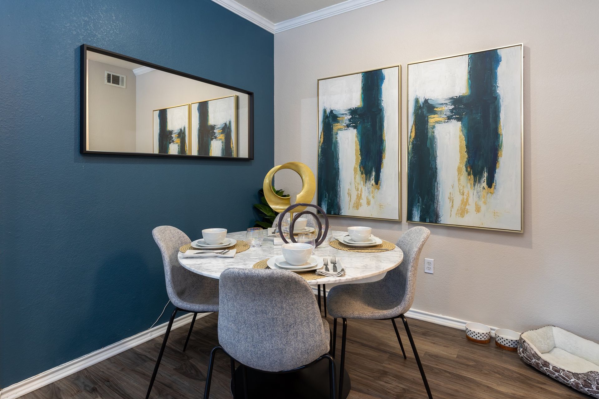Dining area: round marble table with four chairs. Blue and gold abstract art. Dark blue wall.