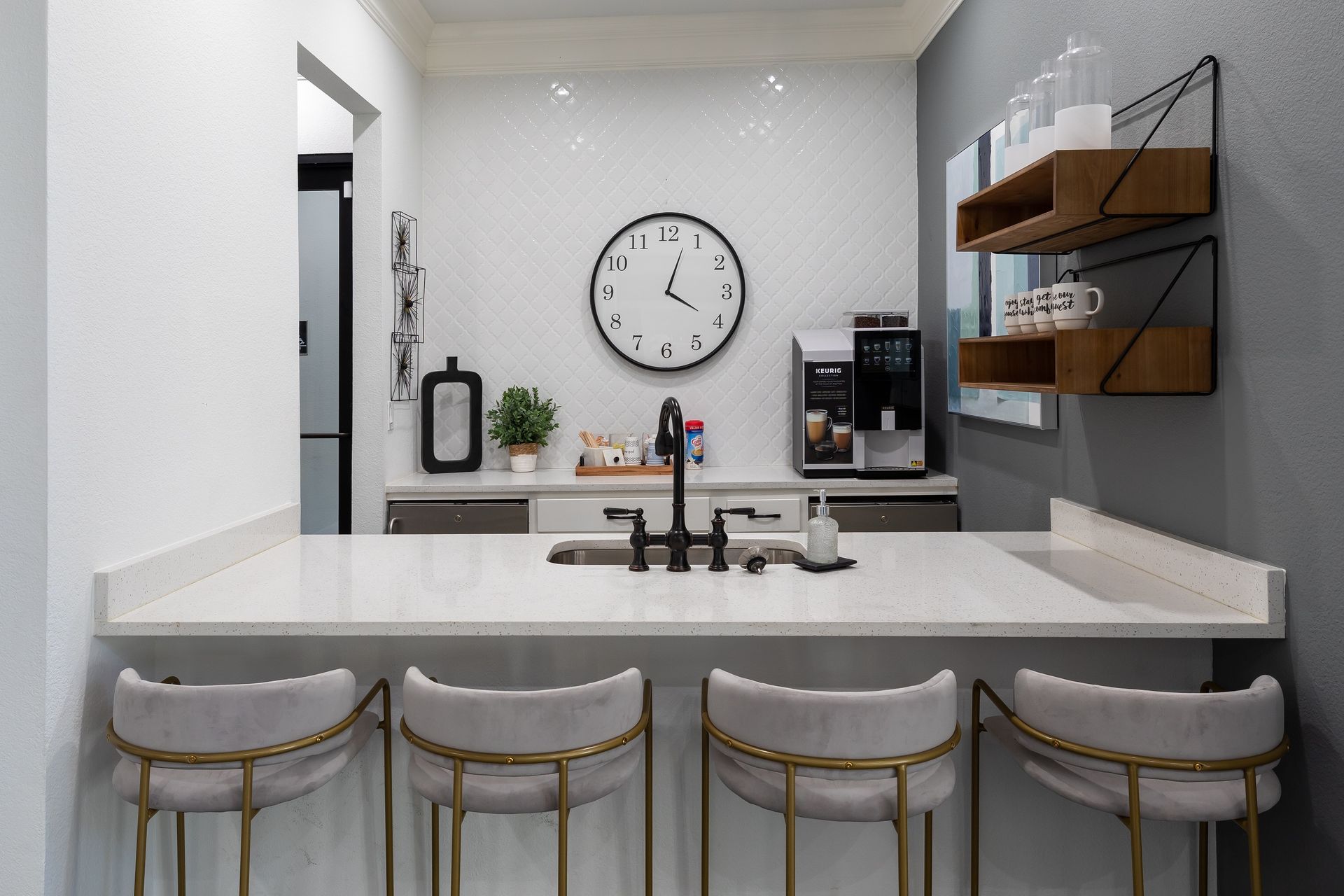 A modern kitchen with bar stools, a white countertop, and a black clock.