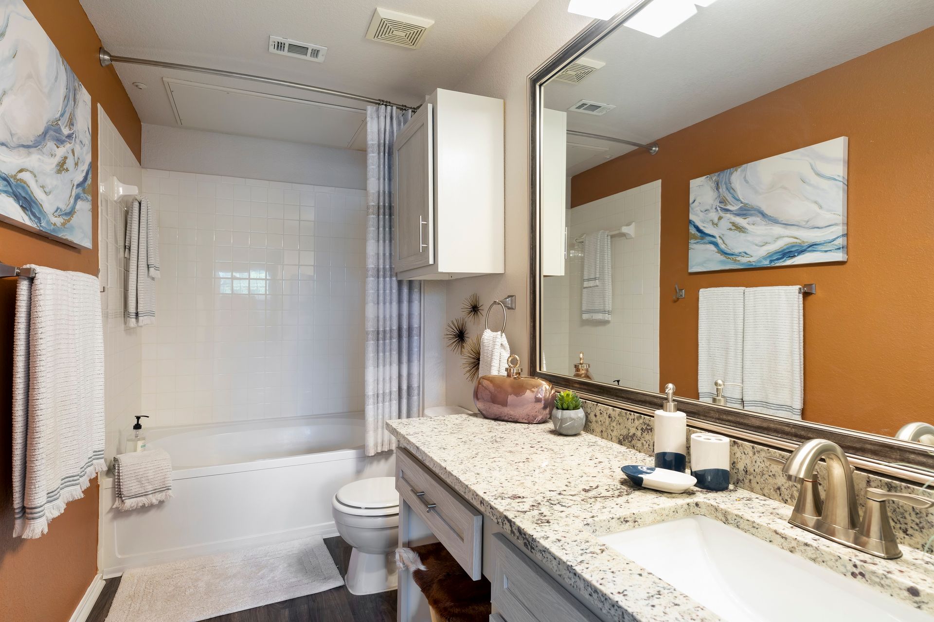 Bathroom with orange walls, white tub, gray vanity, and marble art.