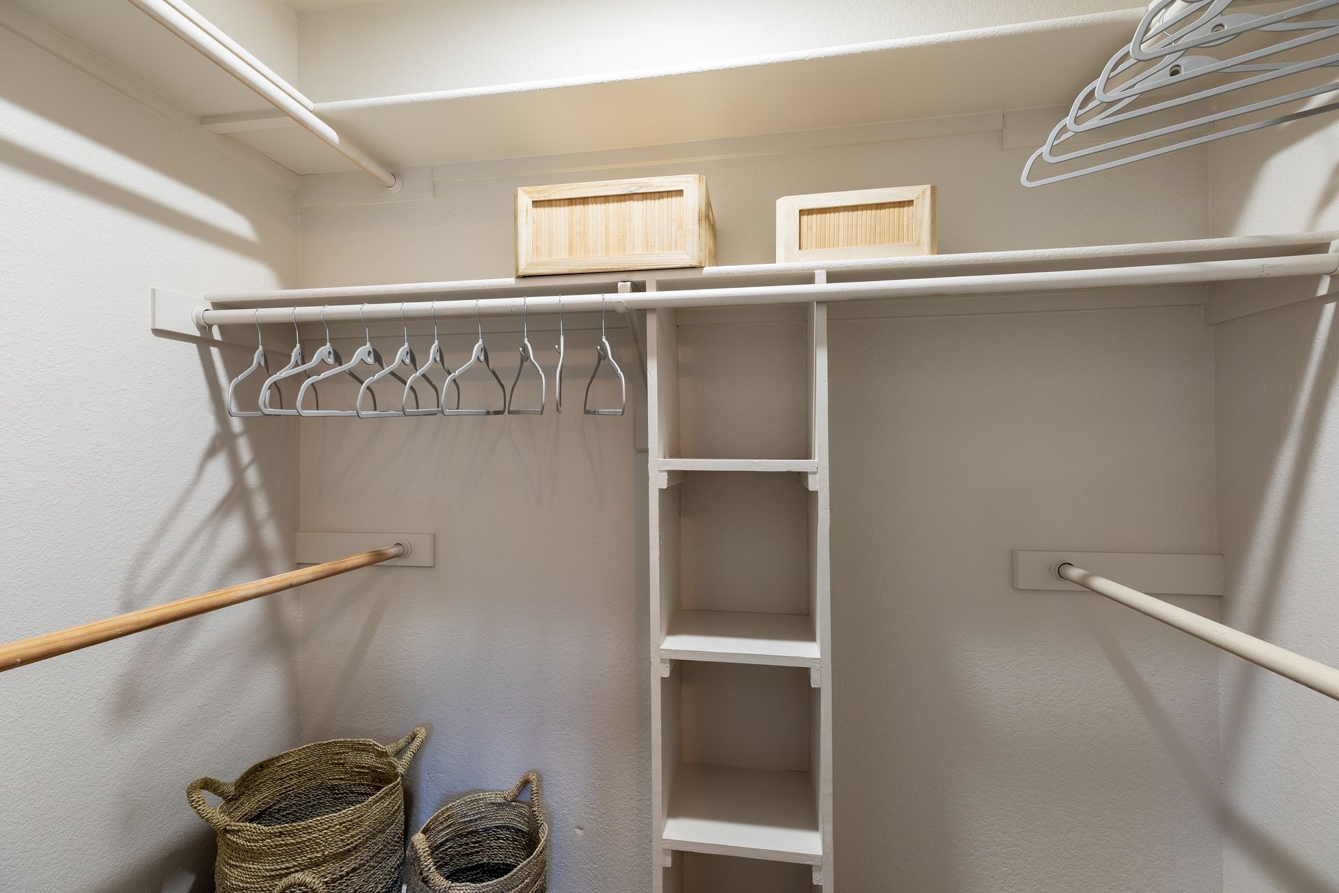 Empty white closet with hanging rods, shelves, and wicker baskets.