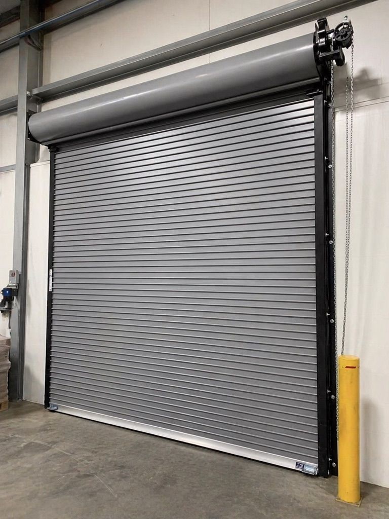 Closed gray metal roll-up warehouse door with black side rails and yellow safety bollard nearby