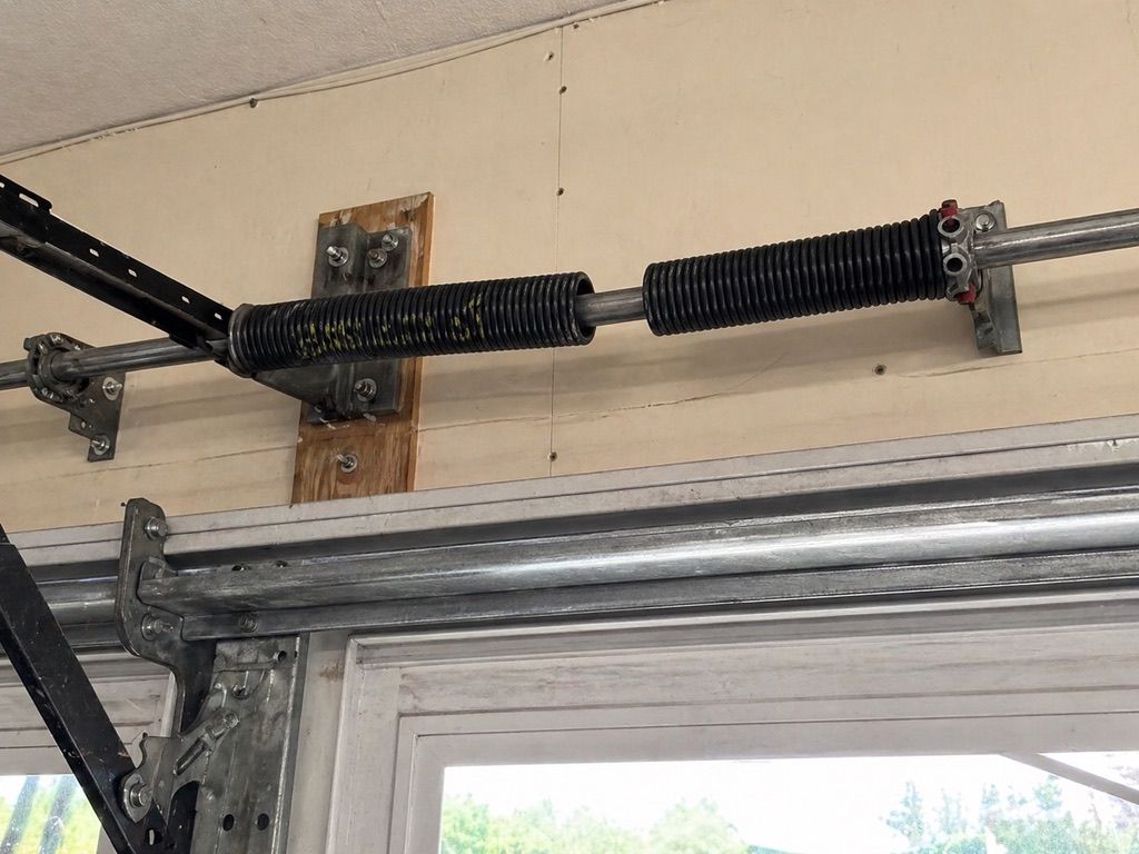 Garage door torsion spring assembly mounted above a white garage door.