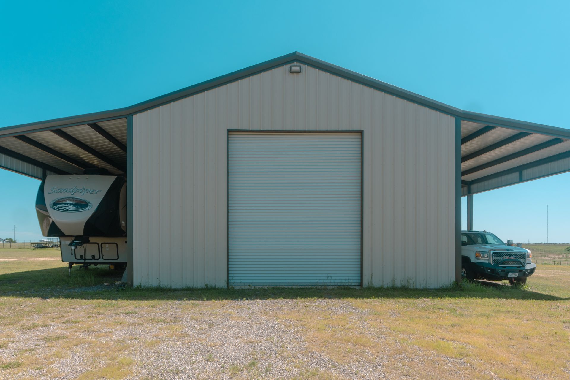 Metal barn with a large roll-up door, truck and trailer on one side, and a car on the other.