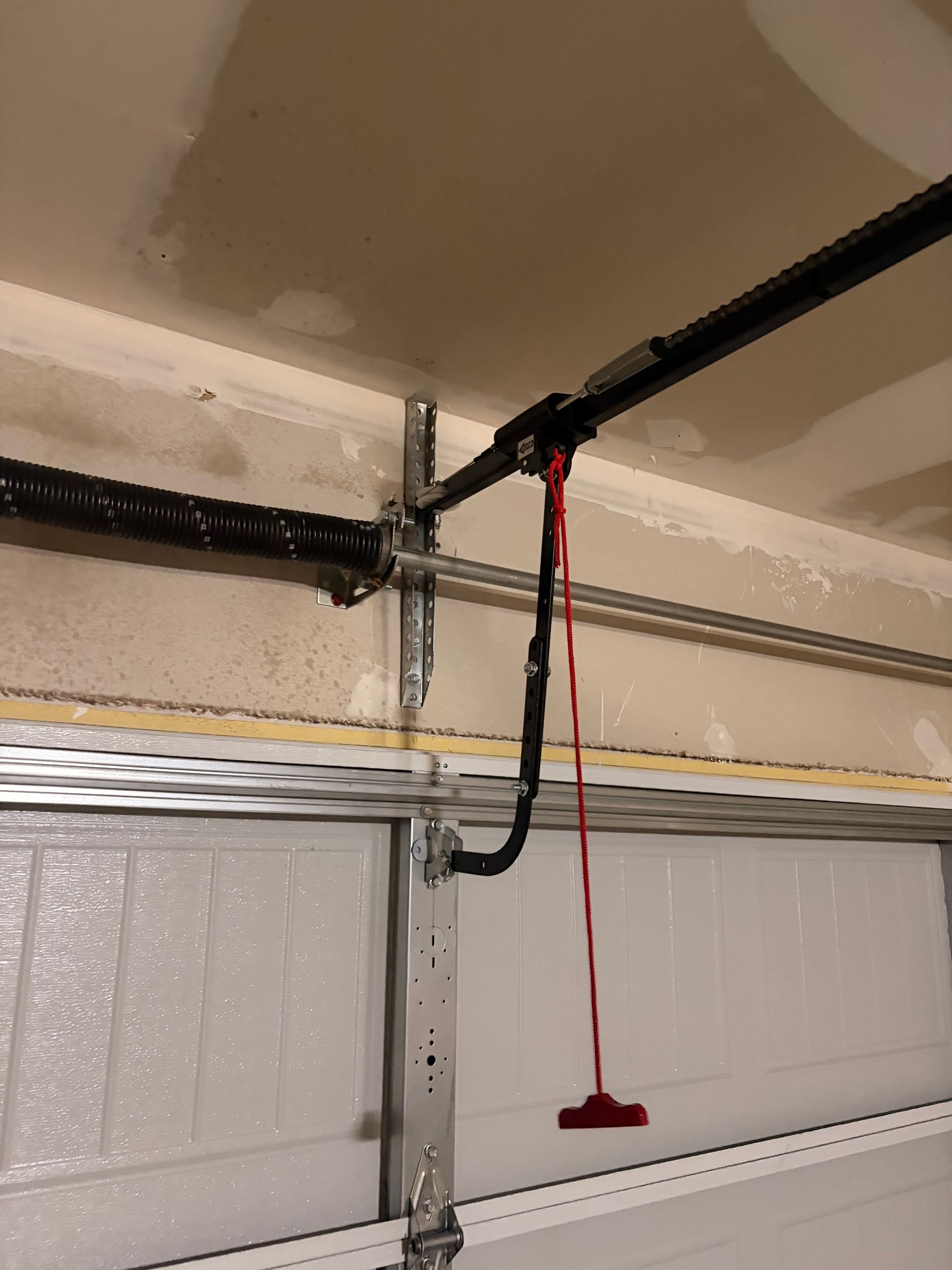 Garage ceiling with a garage door opener rail, hanging red release cord, and white sectional door.