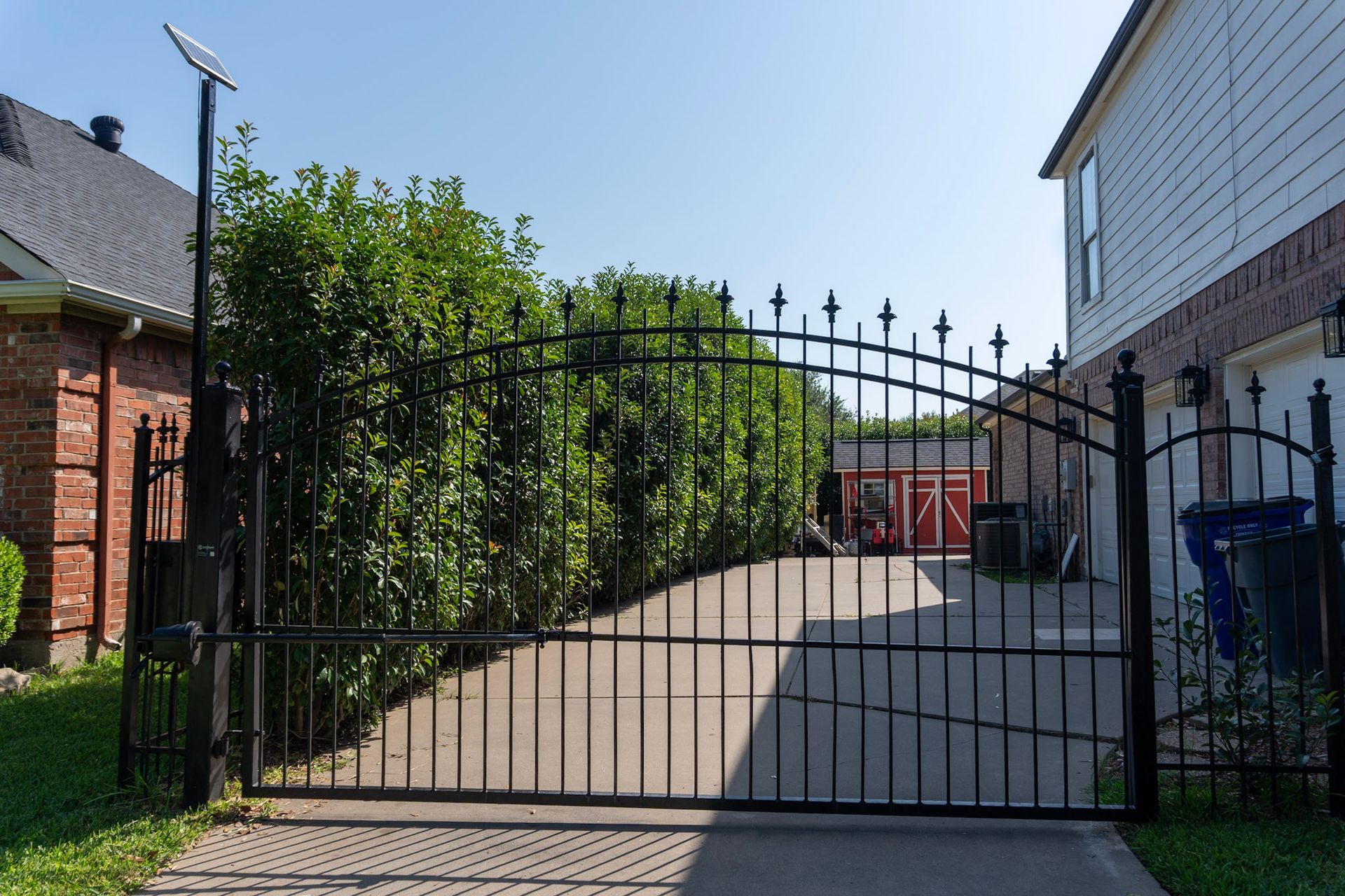 Black metal gate blocking a paved driveway between houses on a sunny day