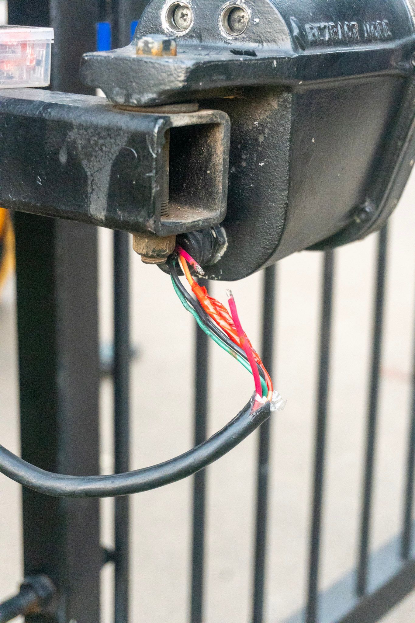 Close-up of a broken black metal fixture with exposed red and green wires hanging out.