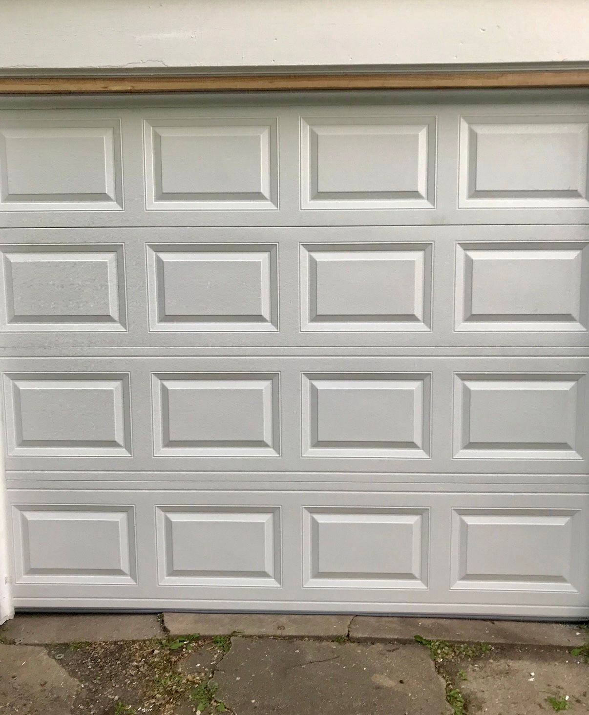 White paneled garage door with four rows of rectangular windows, above a stone driveway.
