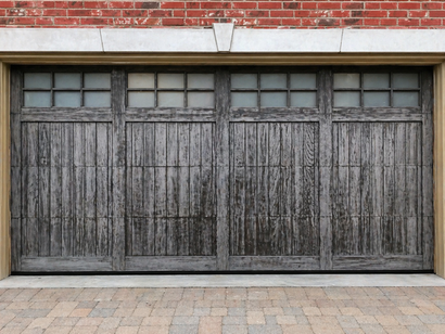 Weathered gray wooden garage doors beneath a red brick wall and concrete driveway