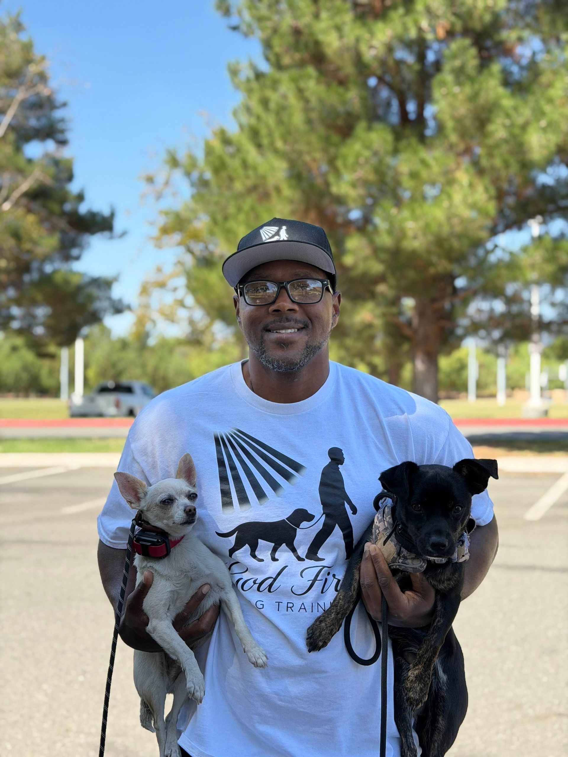 Man in white shirt holds two dogs in a park.