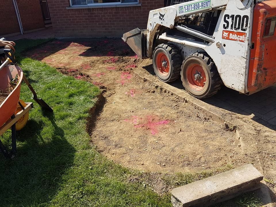 Bobcat skid steer removes dirt from a yard, creating a garden bed.