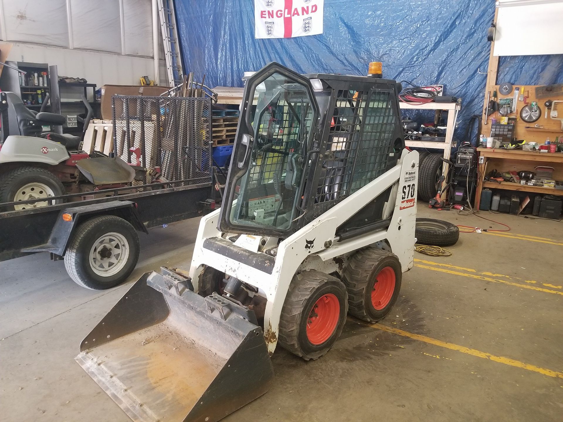 A bobcat skid steer is parked in a garage next to a golf cart.