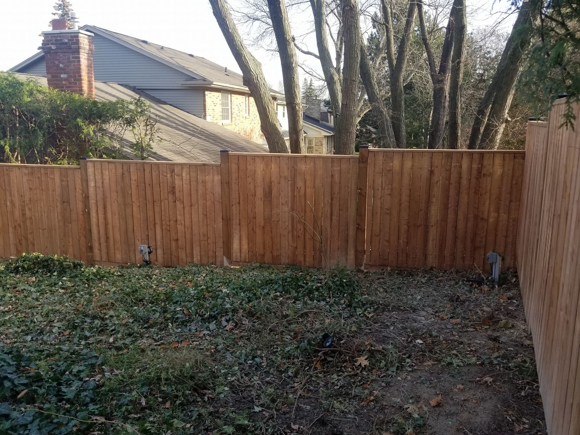 A backyard enclosed by a wooden fence, with a house and bare trees in the background.