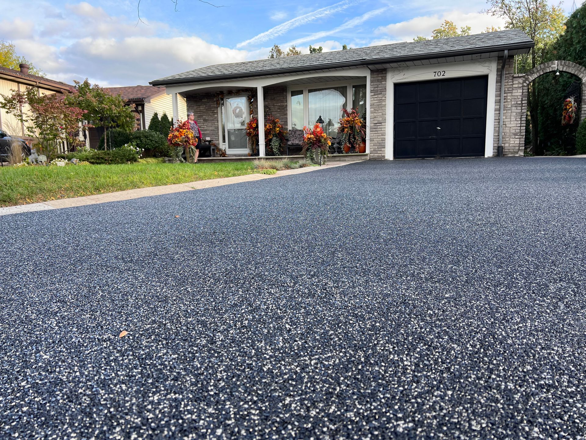 Driveway leading to a bungalow with a black garage door, blue sky above.